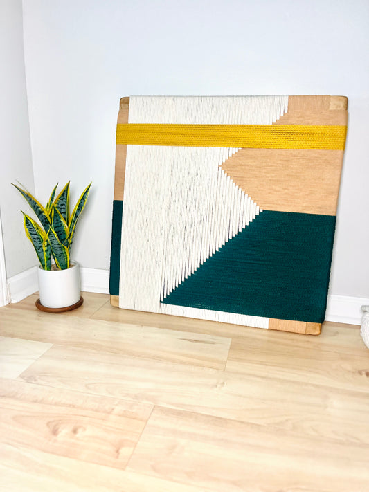 a wooden frame with a colorful abstract design, placed on a wooden floor next to a potted plant.