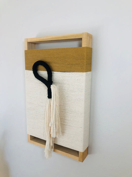 a wooden frame with a woven fabric panel inside, hanging on a white wall.