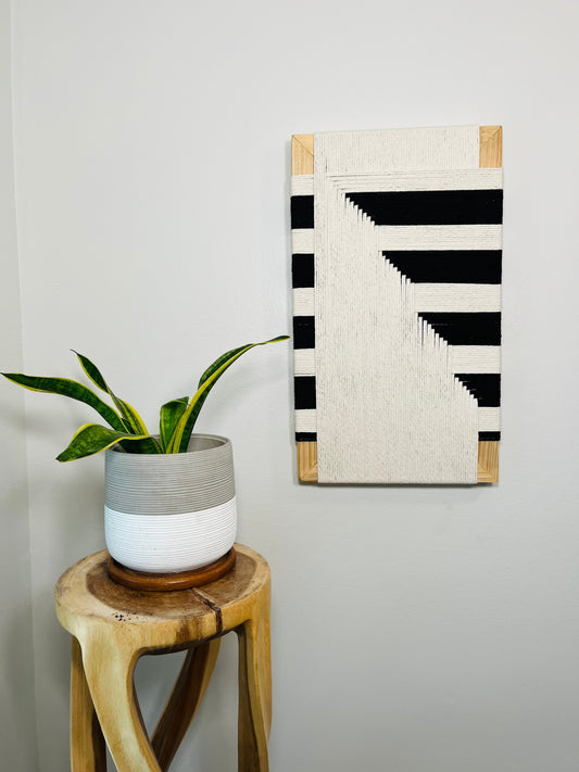 a potted plant on a wooden stool, with a framed artwork hanging on the wall next to it.