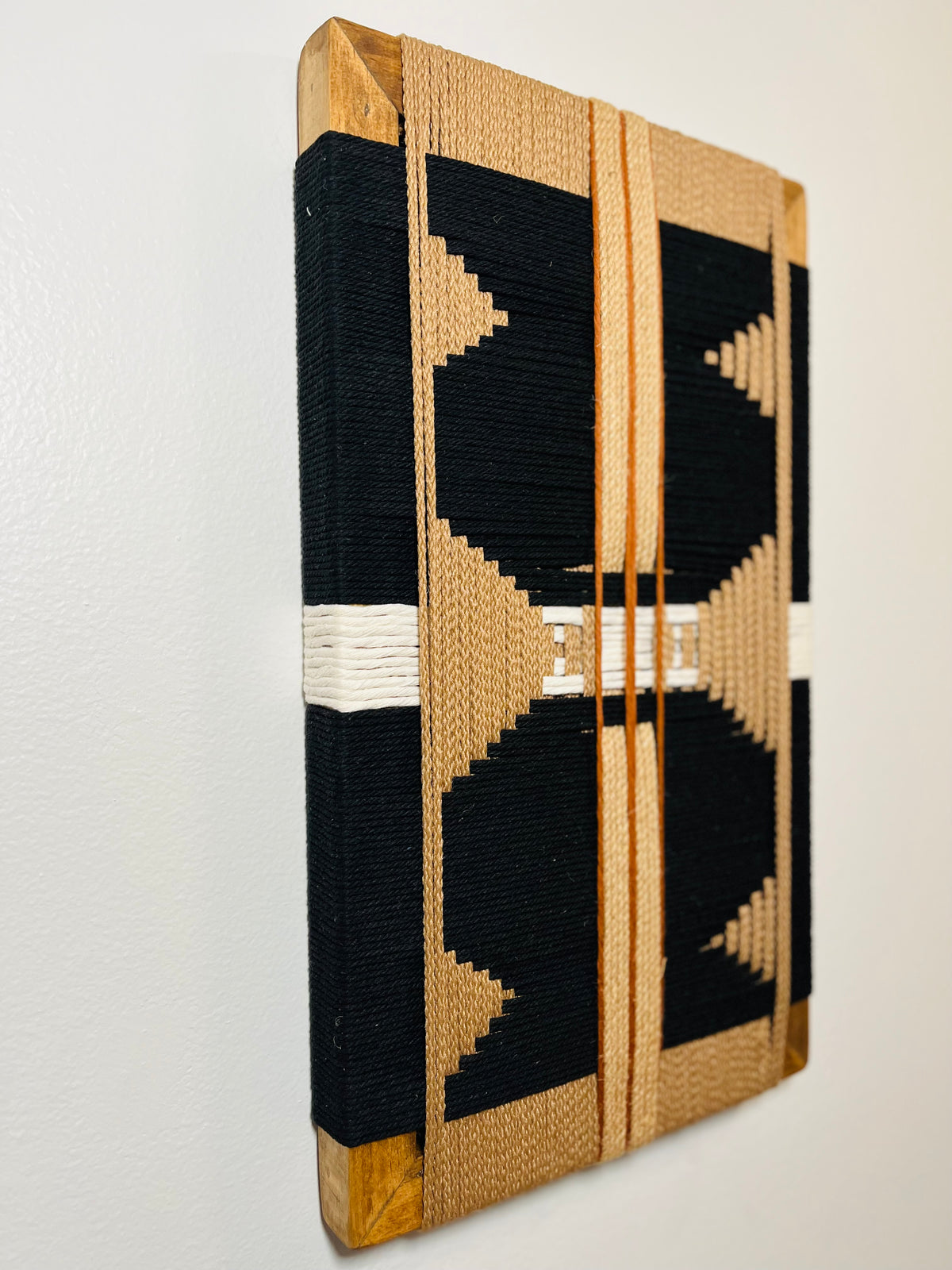 a piece of wall art with a striking black and white geometric pattern. The artwork is displayed on a white wall, and it appears to be a framed piece of wall decor.
