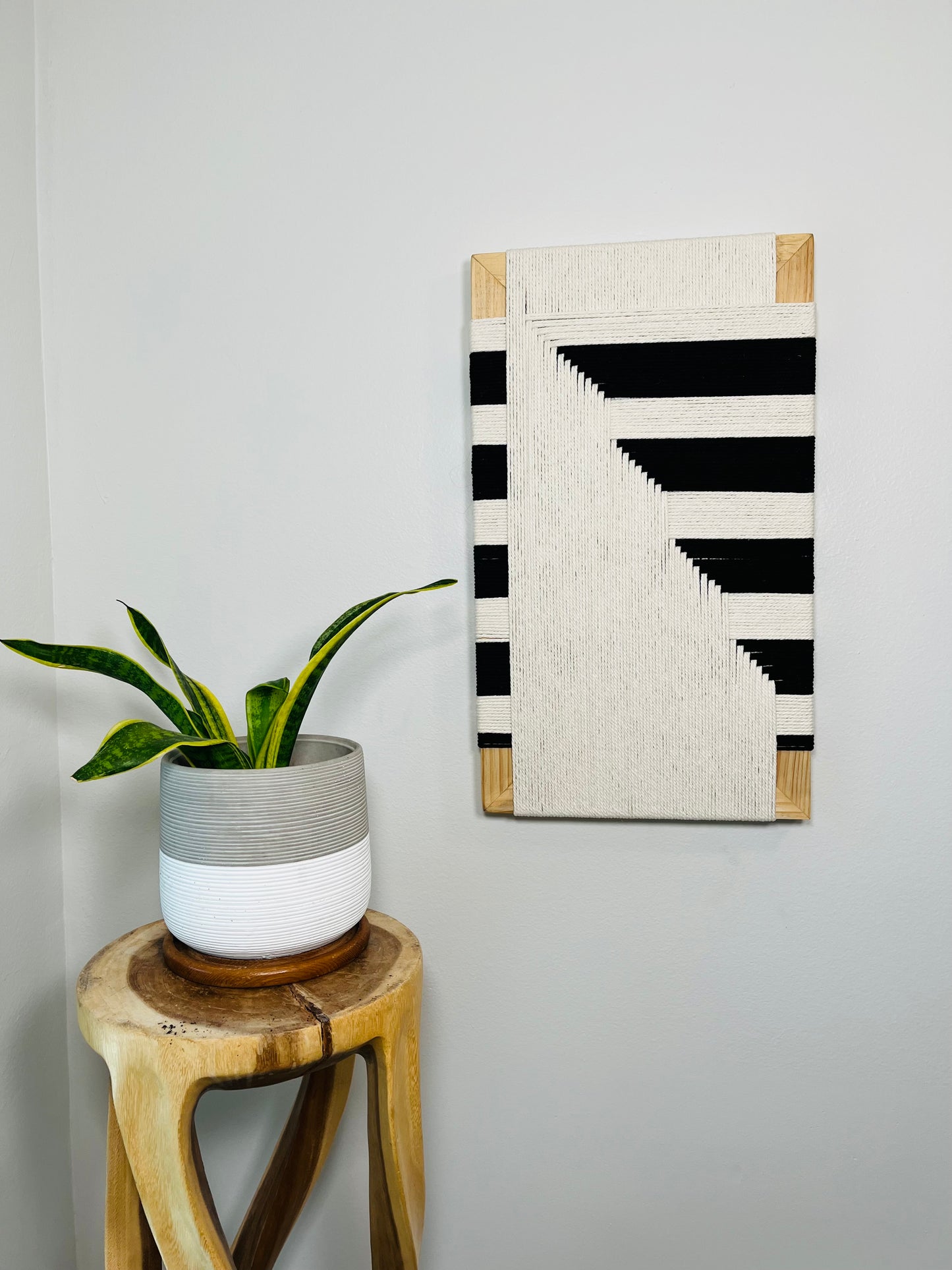 a potted plant on a wooden stool, with a framed abstract artwork hanging on the wall next to it.