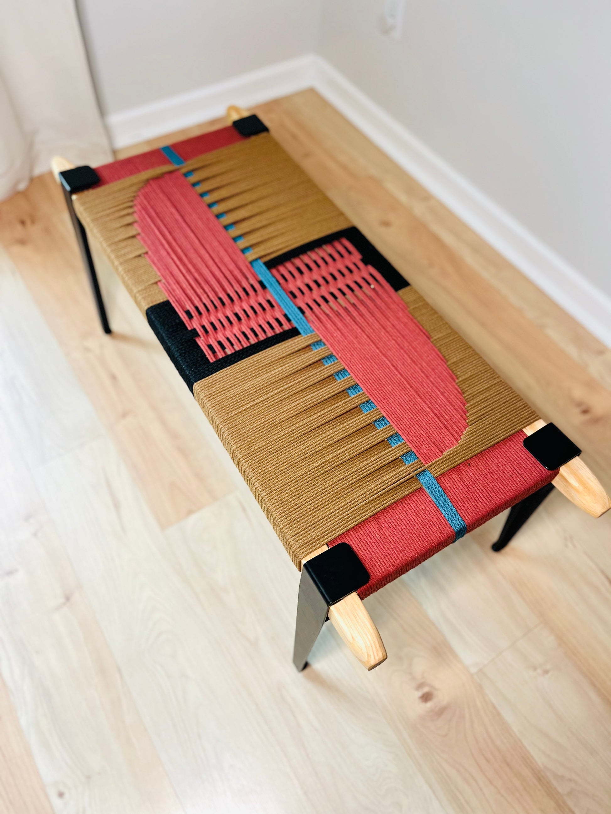 a bench with a unique, colorful design made of woven materials. The bench has a striking combination of red, blue, and brown colors, creating a visually appealing and modern aesthetic.