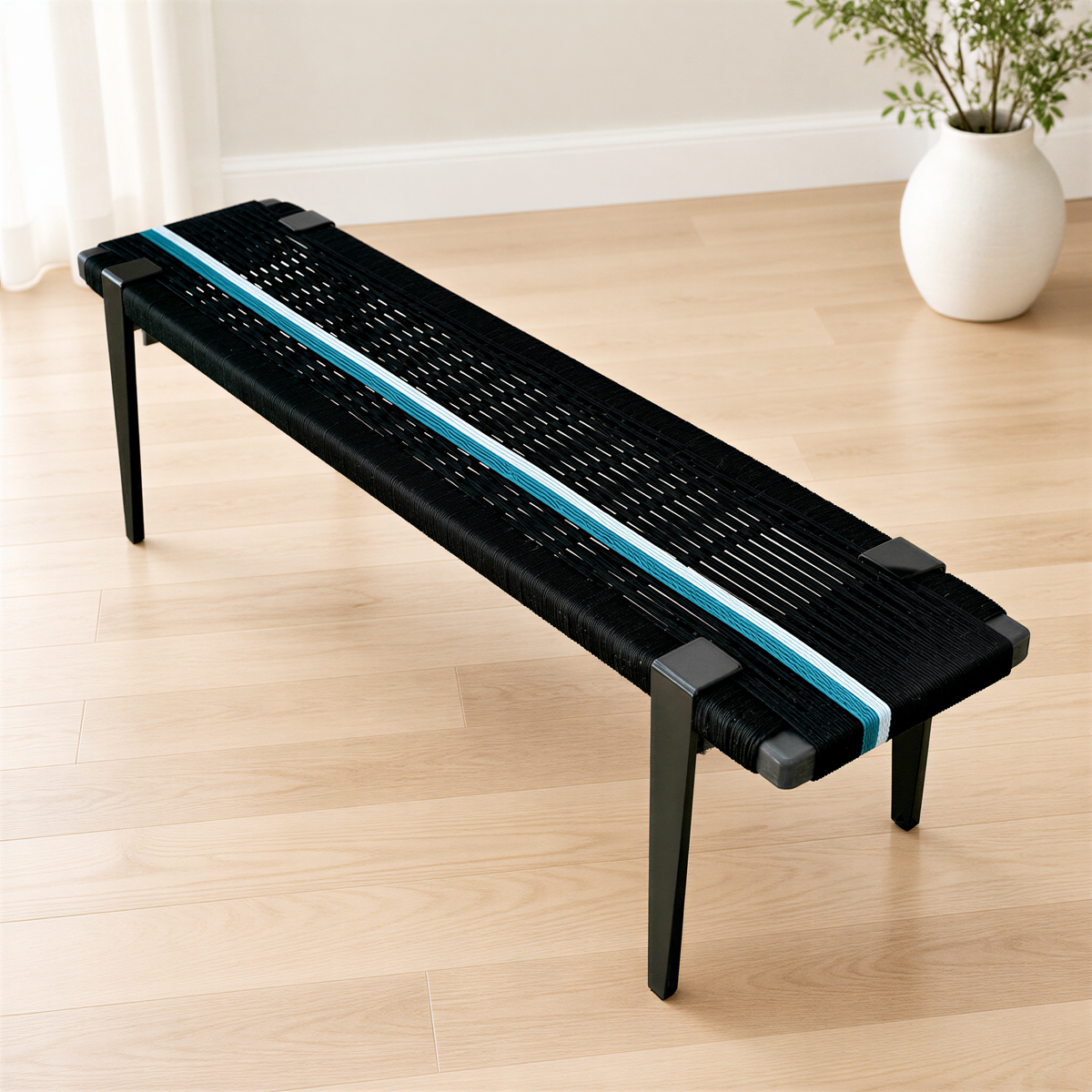 A black bench with a blue stripe on the seat is placed on a wooden floor in a room with a white wall and a plant in a white pot.