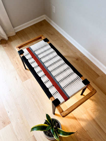 a wooden bench with a woven seat and a red stripe, placed on a wooden floor. There is a potted plant nearby, adding a touch of greenery to the scene.