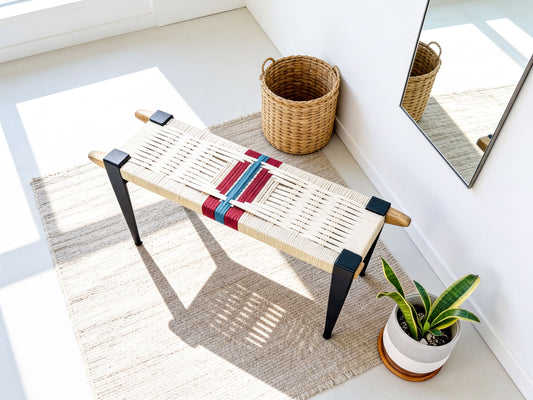 a woven bench with a woven basket and a potted plant placed on a beige rug in a bright, airy room.