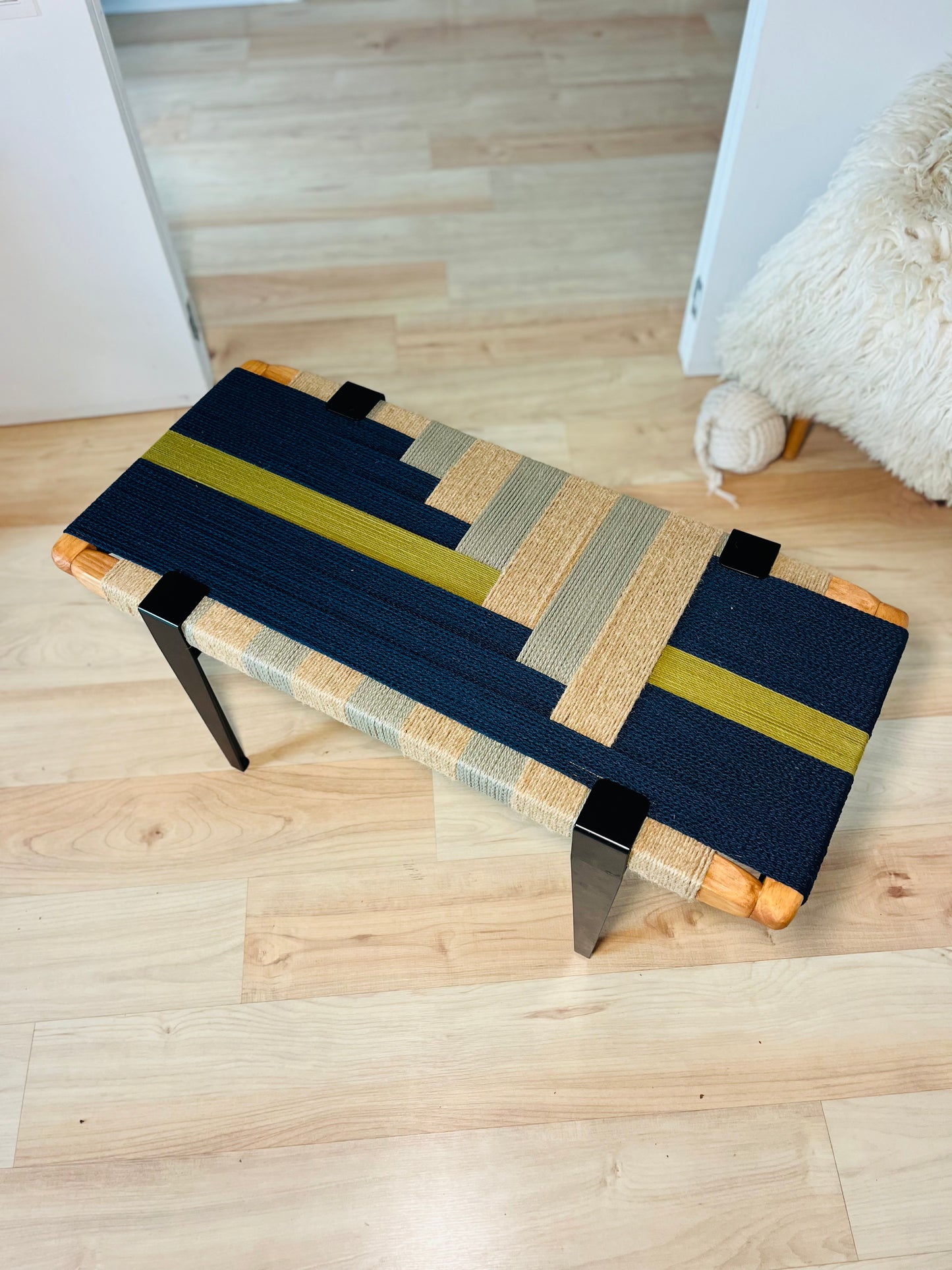 a wooden bench with a woven seat and legs, placed on a wooden floor.