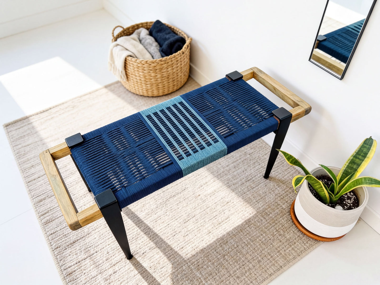 a blue woven bench with a wooden frame, placed on a beige rug in a room with a mirror and a potted plant nearby.