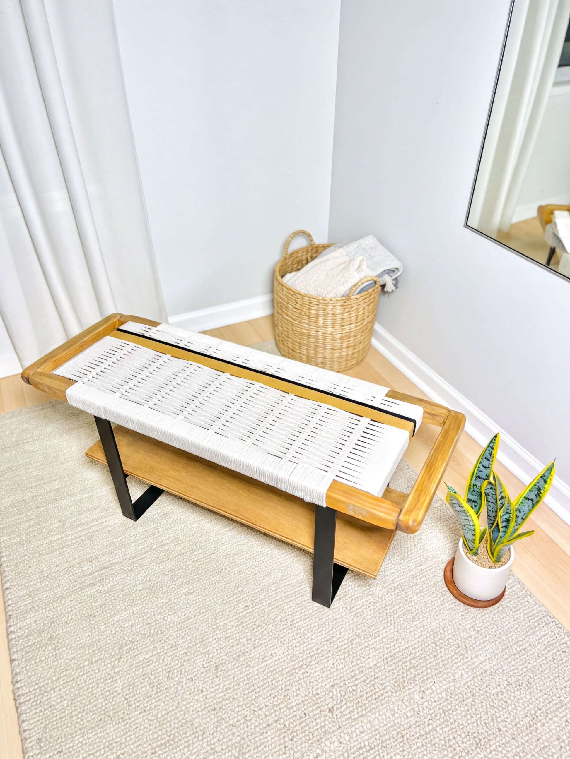 a modern, minimalist living space with a wooden bench, a woven basket, and a potted plant.