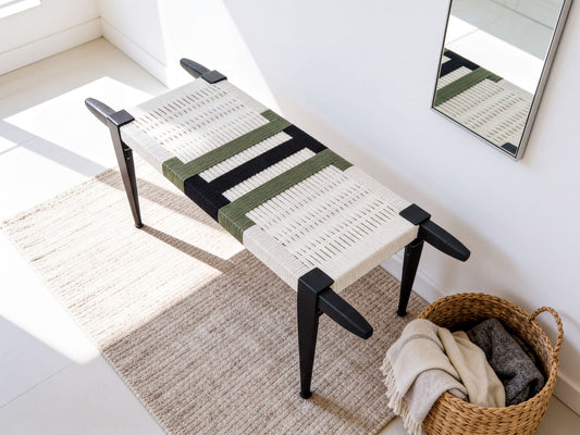 a woven bench with a white and green striped seat, placed on a beige rug next to a woven basket filled with clothes.