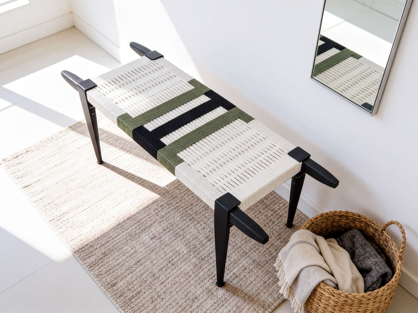 a woven bench with a white and green striped seat, placed on a beige rug next to a woven basket filled with clothes.