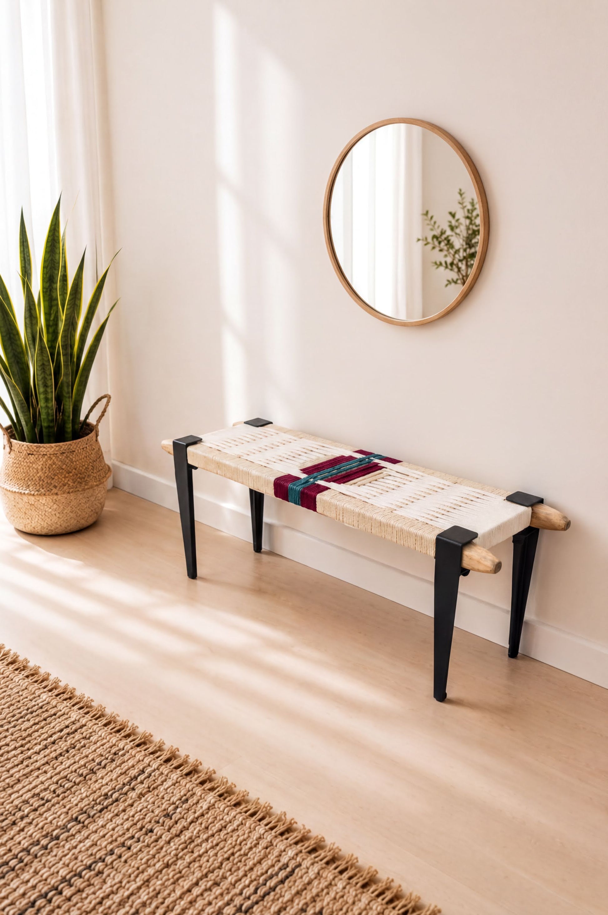 a modern, minimalist living space with a round mirror on the wall, a woven bench with black legs, and a potted plant on the floor.
