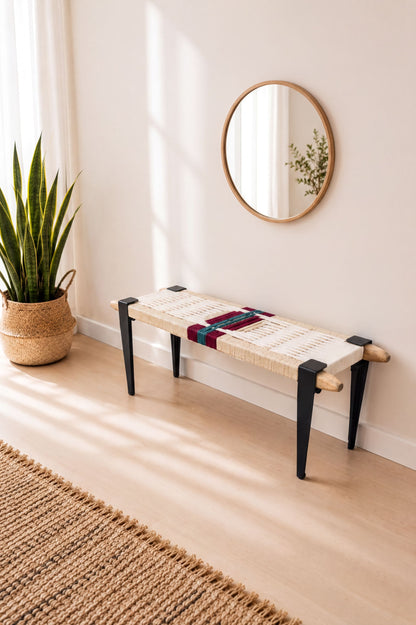 a modern, minimalist living space with a round mirror on the wall, a woven bench with black legs, and a potted plant on the floor.
