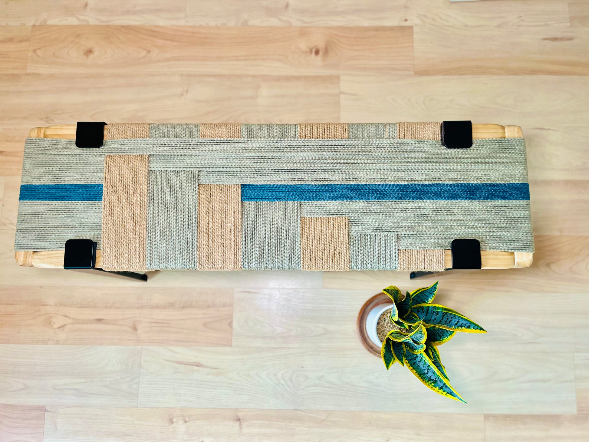 a wooden bench with a woven seat and a small potted plant placed on the floor next to it.