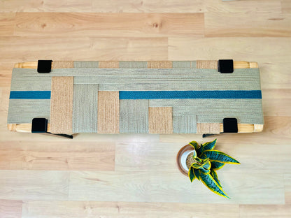 a wooden bench with a woven seat and a small potted plant placed on the floor next to it.