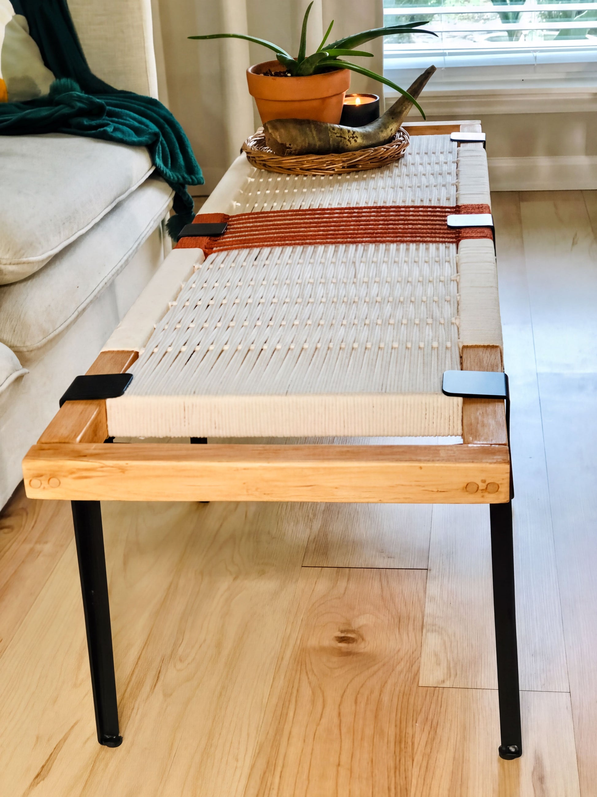 a wooden coffee table with a woven seat and a potted plant on top, placed on a wooden floor in a living room setting.