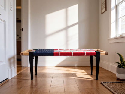 A wooden bench with a red and blue American flag-like design on the seat, placed on a hardwood floor in a room with a white wall and a window.