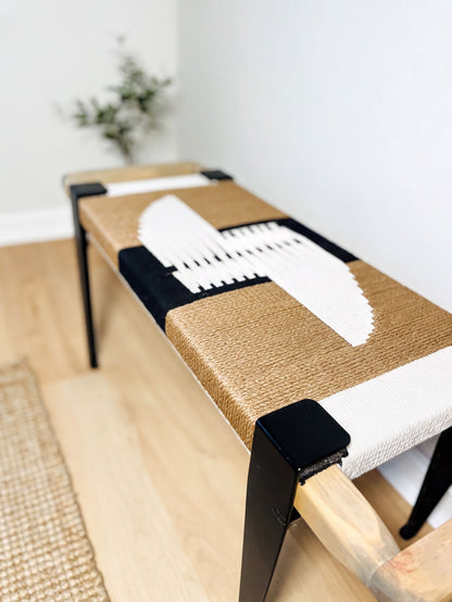 a modern bench with a woven seat and black metal legs, placed on a wooden floor.