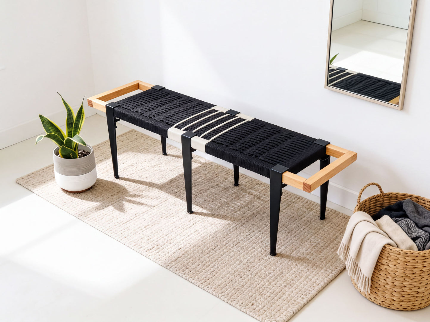 a modern black bench with wooden handles, placed on a beige rug in a room with a mirror and a basket of clothes nearby.