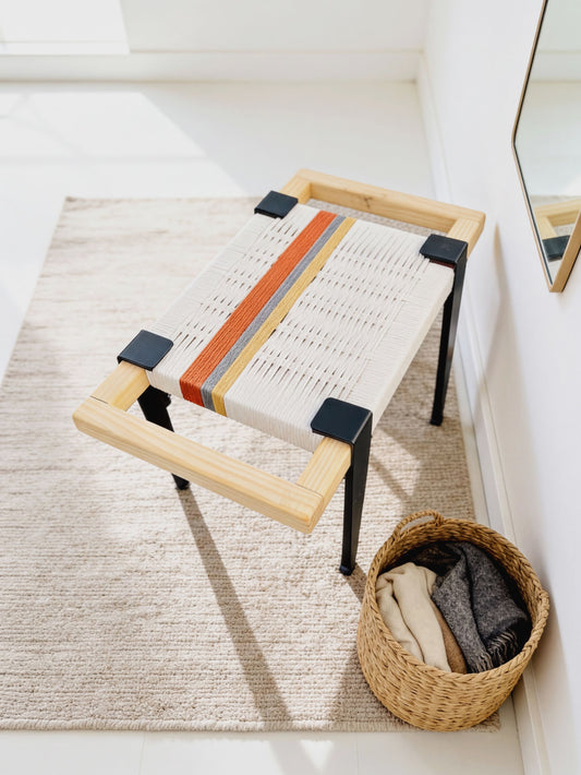 a woven bench with a wooden frame, placed on a beige rug next to a woven basket filled with folded clothes.