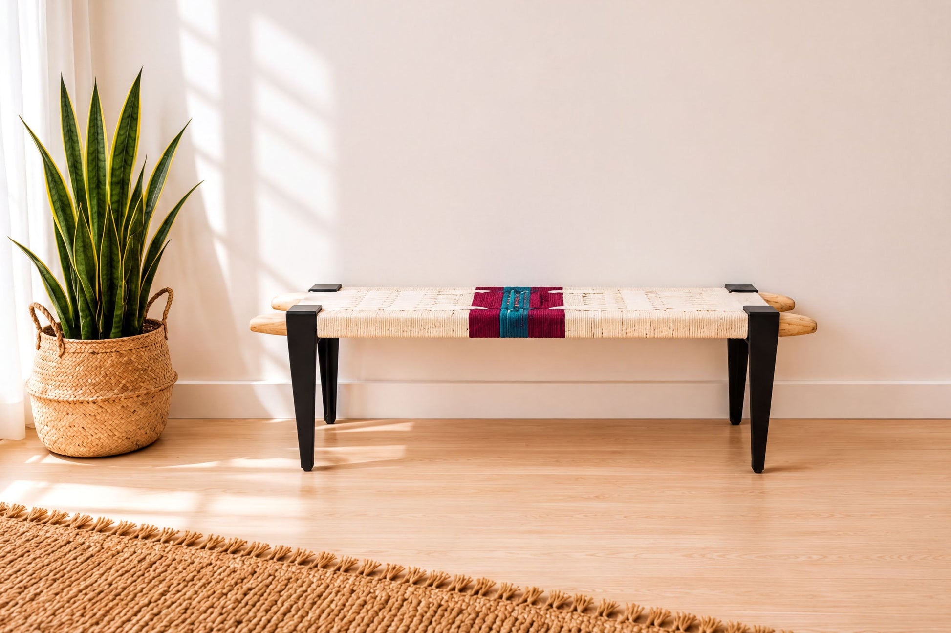 a white bench with a woven seat and black metal legs, placed on a wooden floor next to a potted plant.