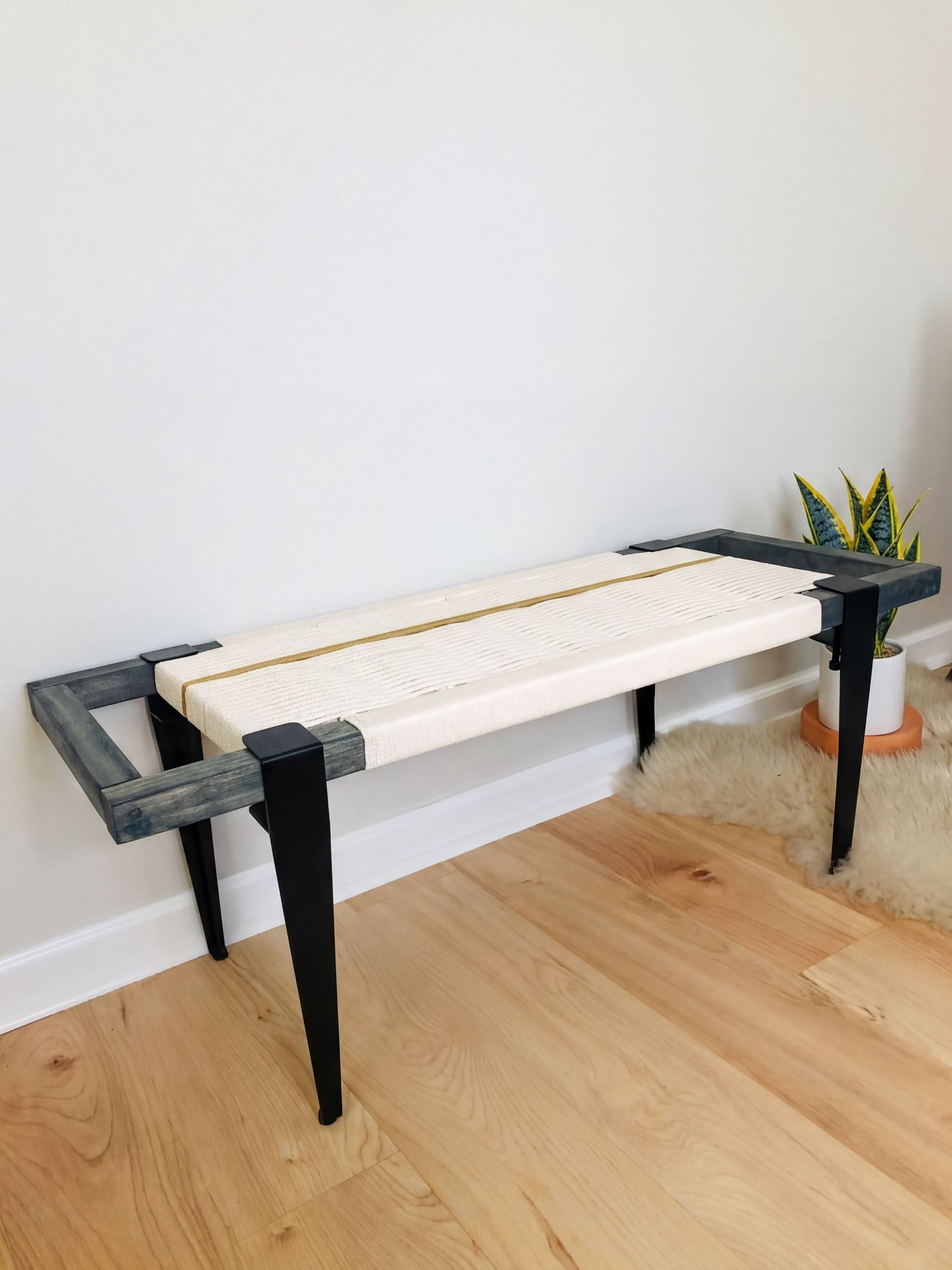 a modern bench with a white seat and black metal legs, placed on a wooden floor against a white wall.