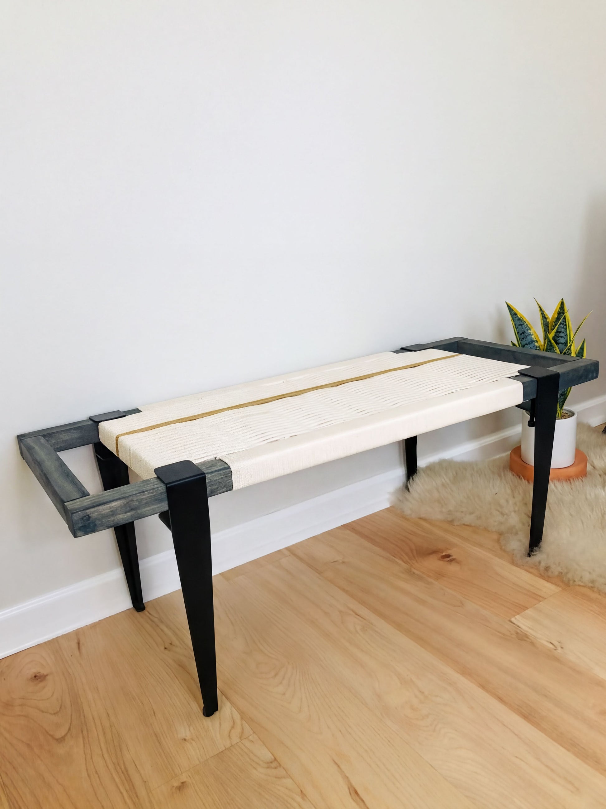 a modern bench with a white seat and black metal legs, placed on a wooden floor against a white wall.