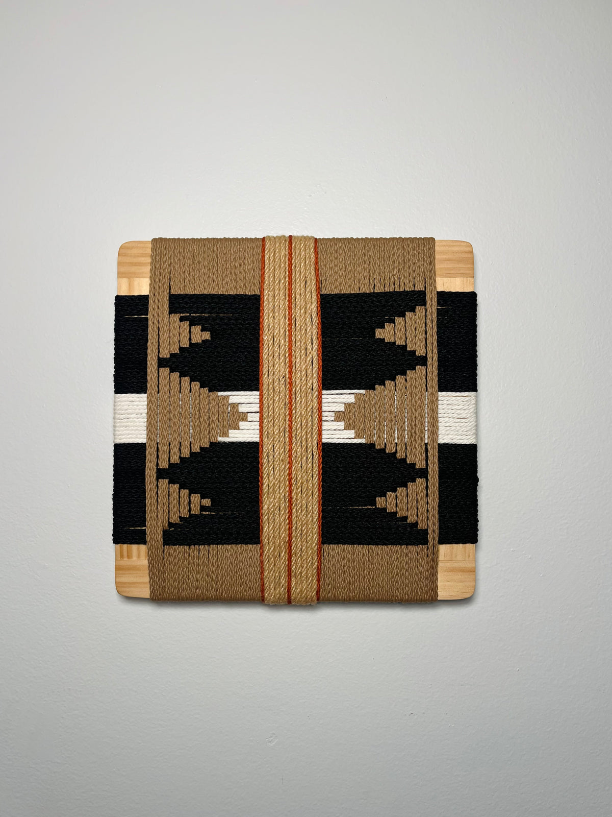 a square-shaped woven textile with a geometric pattern in black, white, and brown colors.