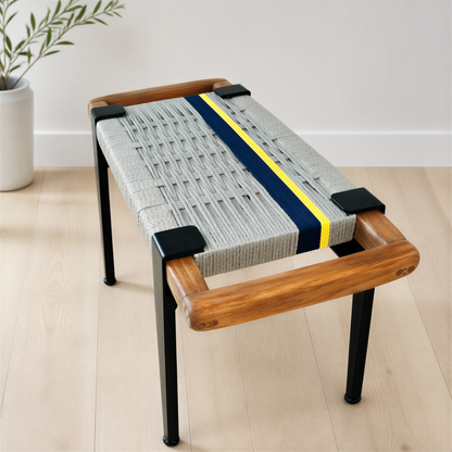 a modern bench with a woven seat and wooden frame, placed on a wooden floor against a white wall.