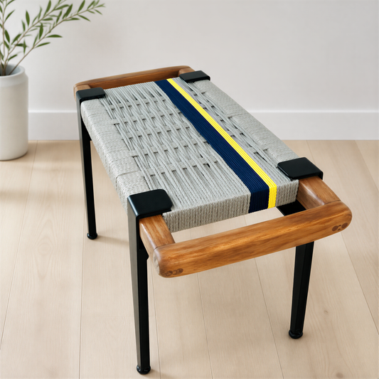 a modern bench with a woven seat and wooden frame, placed on a wooden floor against a white wall.