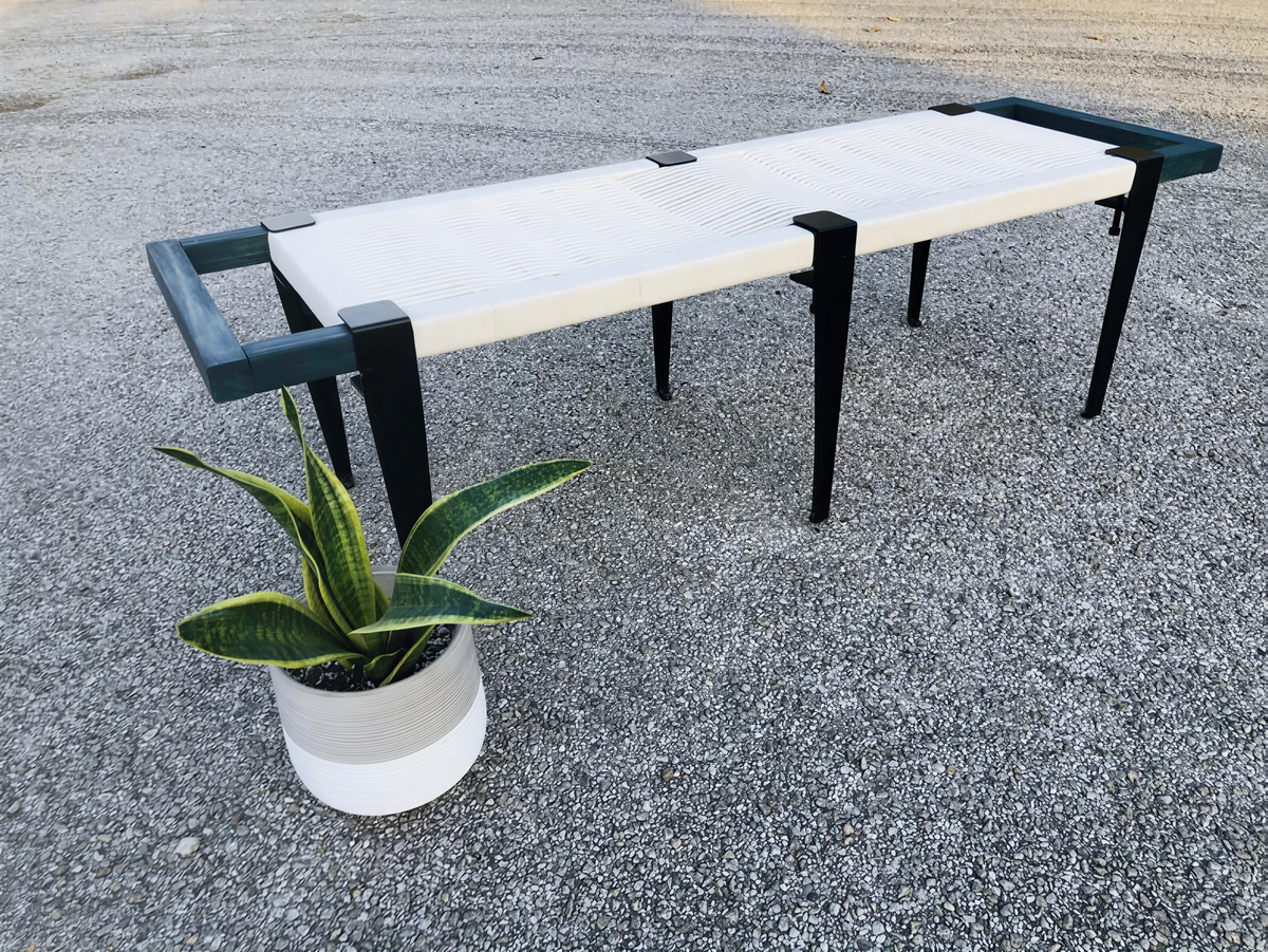 a modern bench with a white seat and black metal legs, placed on a gravel surface next to a potted plant.