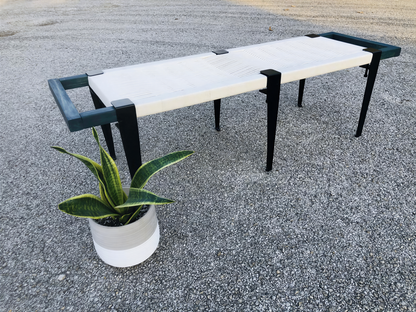 a modern bench with a white seat and black metal legs, placed on a gravel surface next to a potted plant.