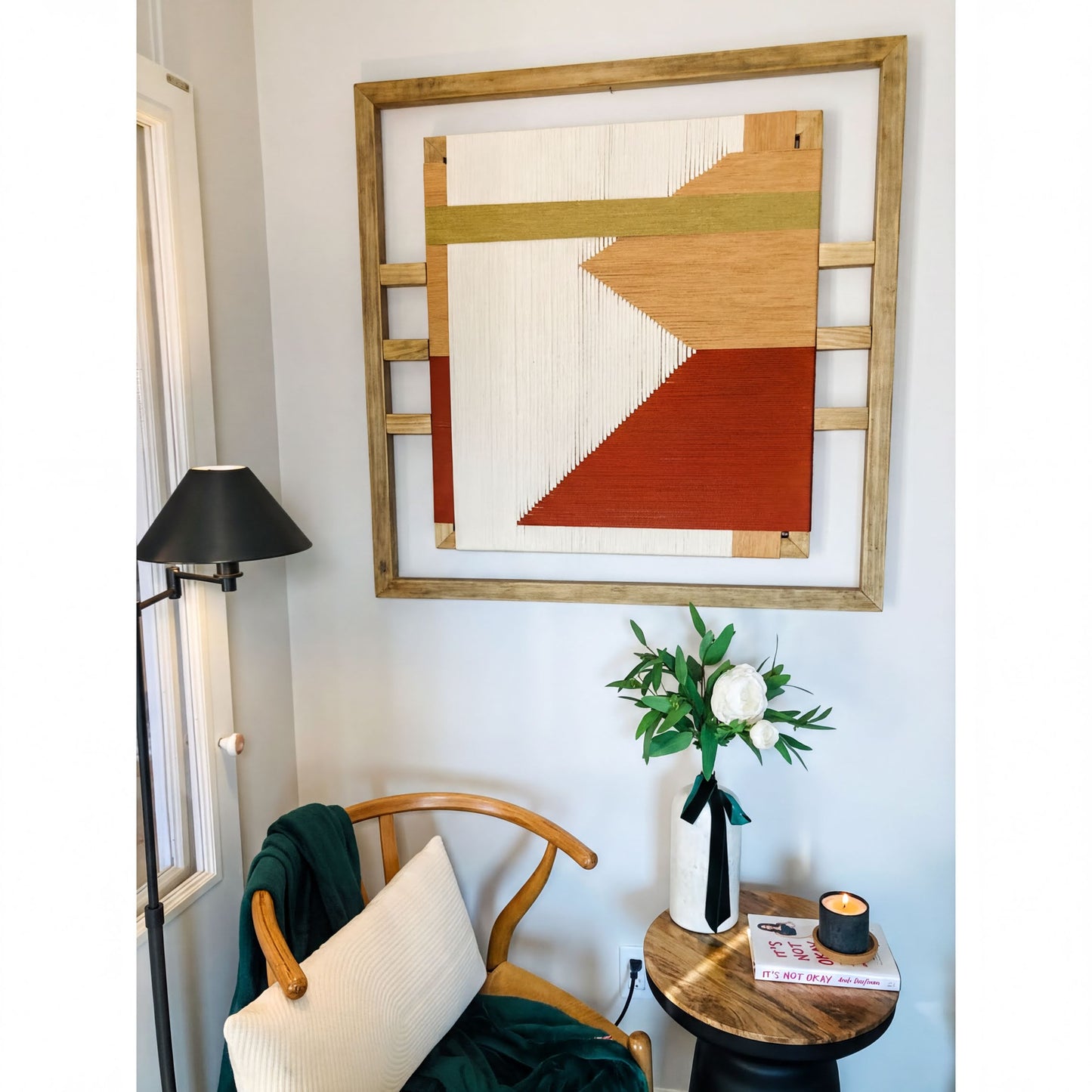 a cozy corner of a room with a wooden chair, a small table with a vase of flowers, and a framed abstract artwork hanging on the wall.