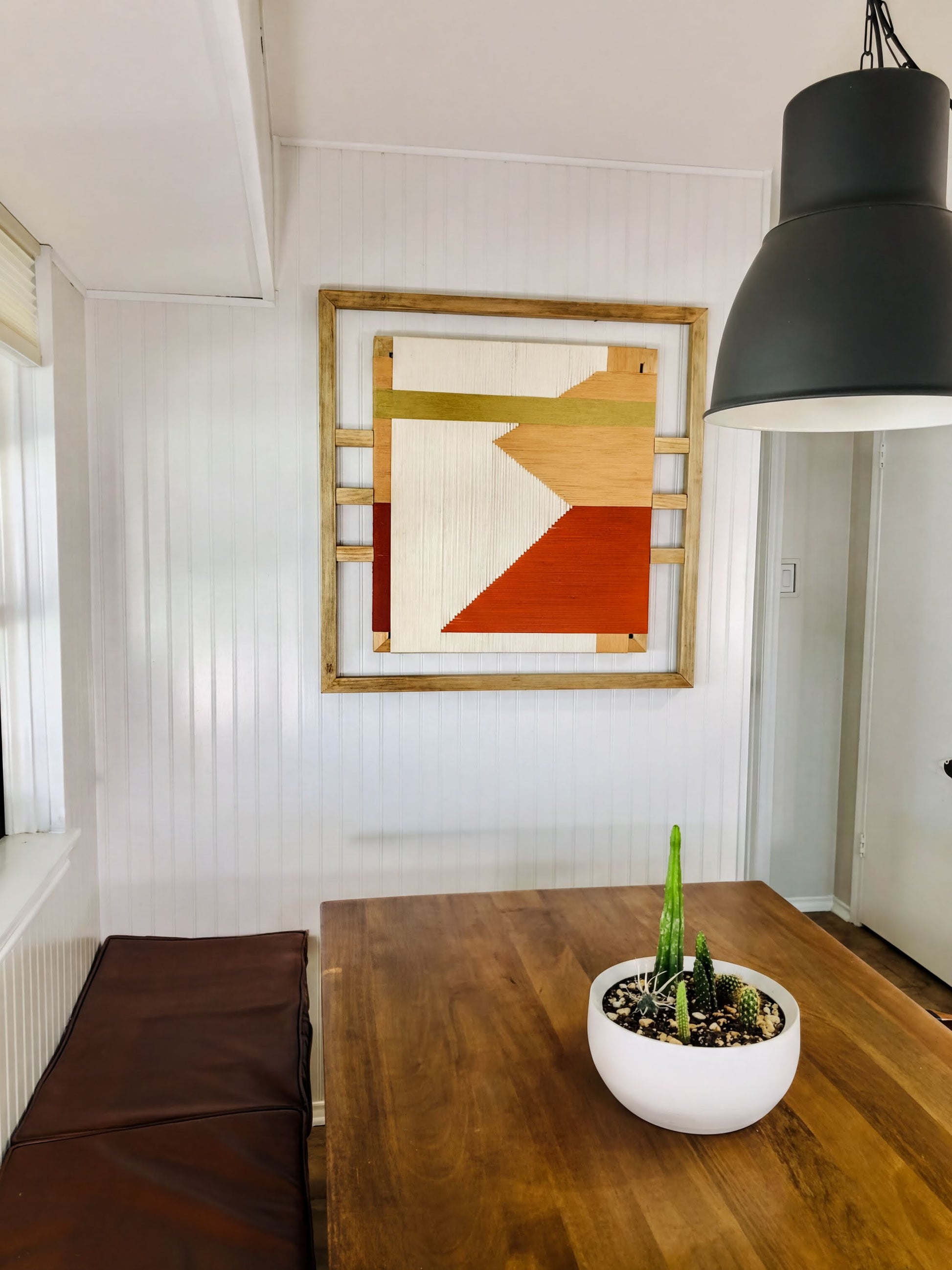 a wooden dining table with a white bowl containing a potted plant, and a framed abstract artwork hanging on the wall above the table.