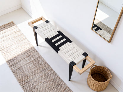 a modern bench with a woven seat and black metal legs, placed on a white floor next to a woven basket.