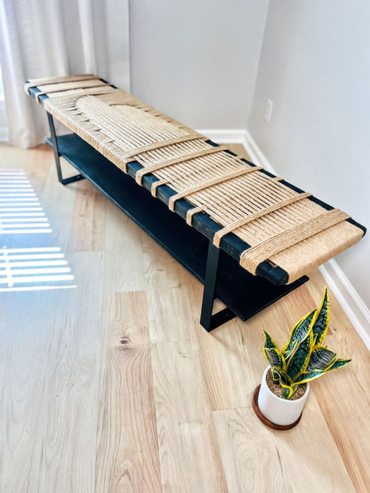 a modern bench with a woven seat and a black metal frame, placed on a wooden floor next to a potted plant.