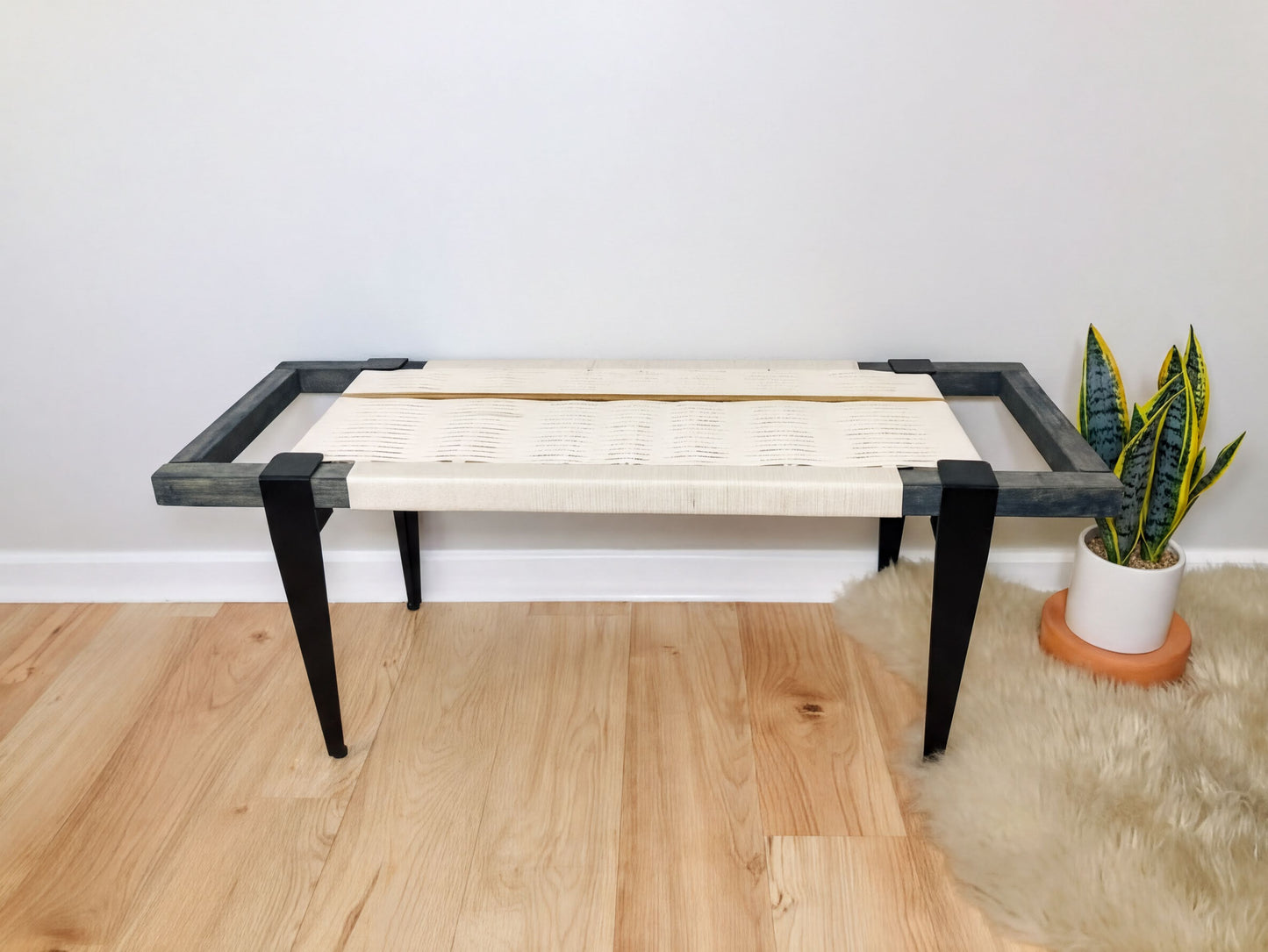 a modern bench with a white seat and black metal frame, placed on a wooden floor next to a potted plant.