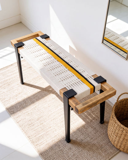 a modern bench with a woven seat and wooden frame, placed on a beige rug in a room with a mirror on the wall.