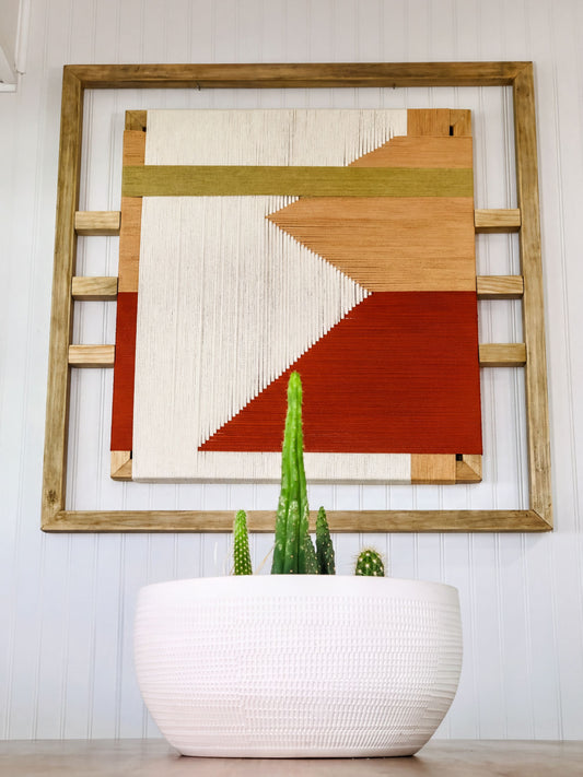 a white planter with a variety of cacti and succulents, placed in front of a wooden frame with a colorful abstract artwork hanging on the wall above it.