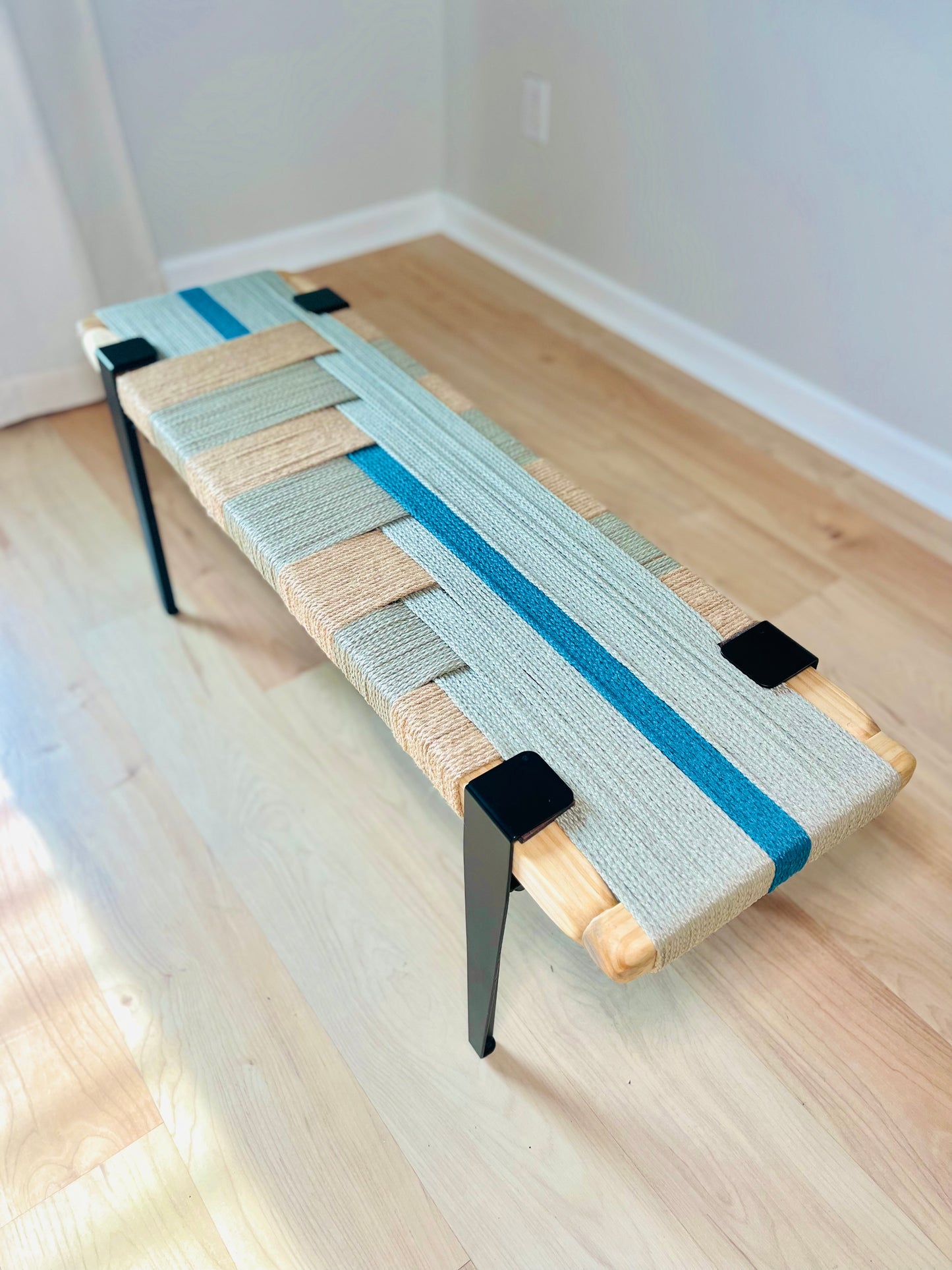 a wooden bench with a woven seat and backrest, placed on a wooden floor. The bench has a unique design with a blue and white striped pattern on the seat and backrest.