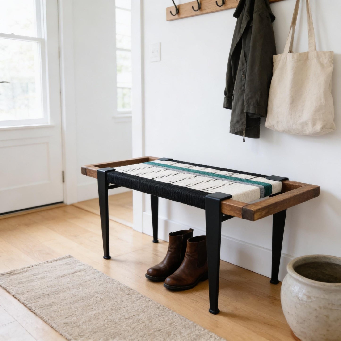 a wooden bench with a woven seat and black metal legs, situated in a hallway with a coat rack and a beige rug.