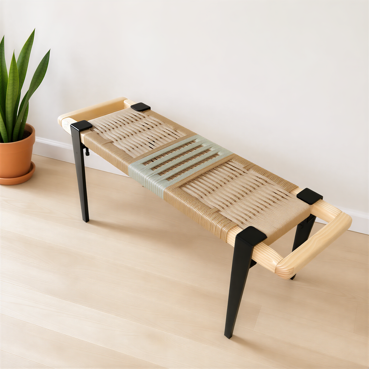 A woven bench with a wooden frame and black metal legs is placed on a wooden floor next to a potted plant.