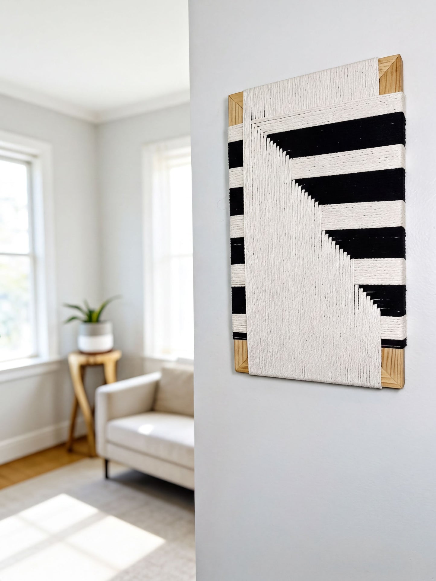 a living room with a white sofa, a wooden side table, and a large abstract artwork featuring black and white stripes hanging on the wall.