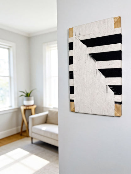 a living room with a white sofa, a wooden side table, and a large abstract artwork featuring black and white stripes hanging on the wall.