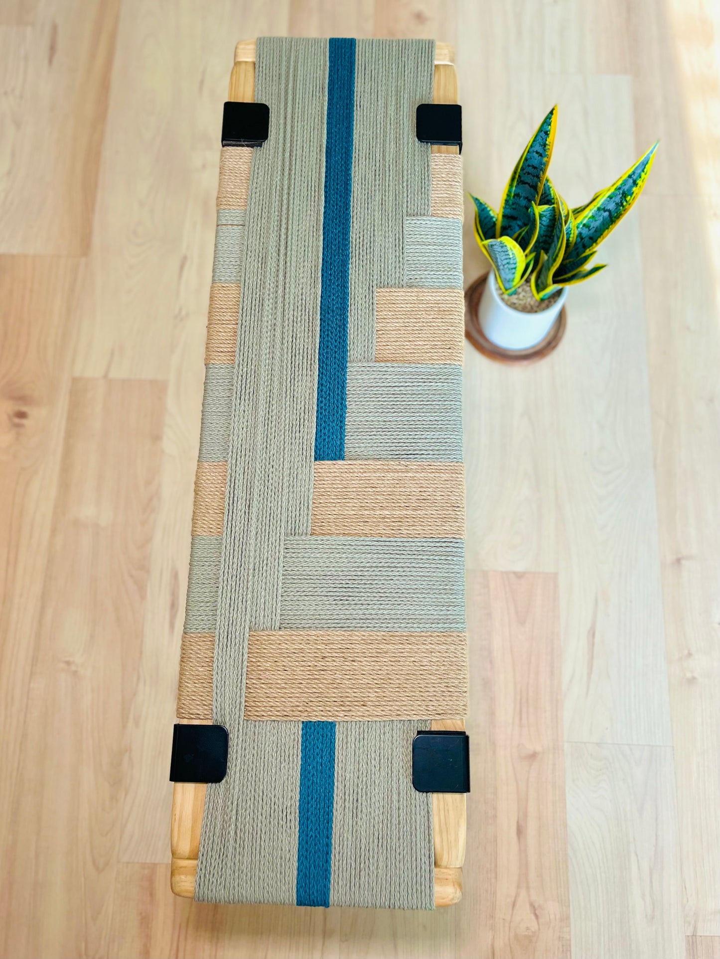 a wooden bench with a woven seat and a potted plant placed on a wooden floor.