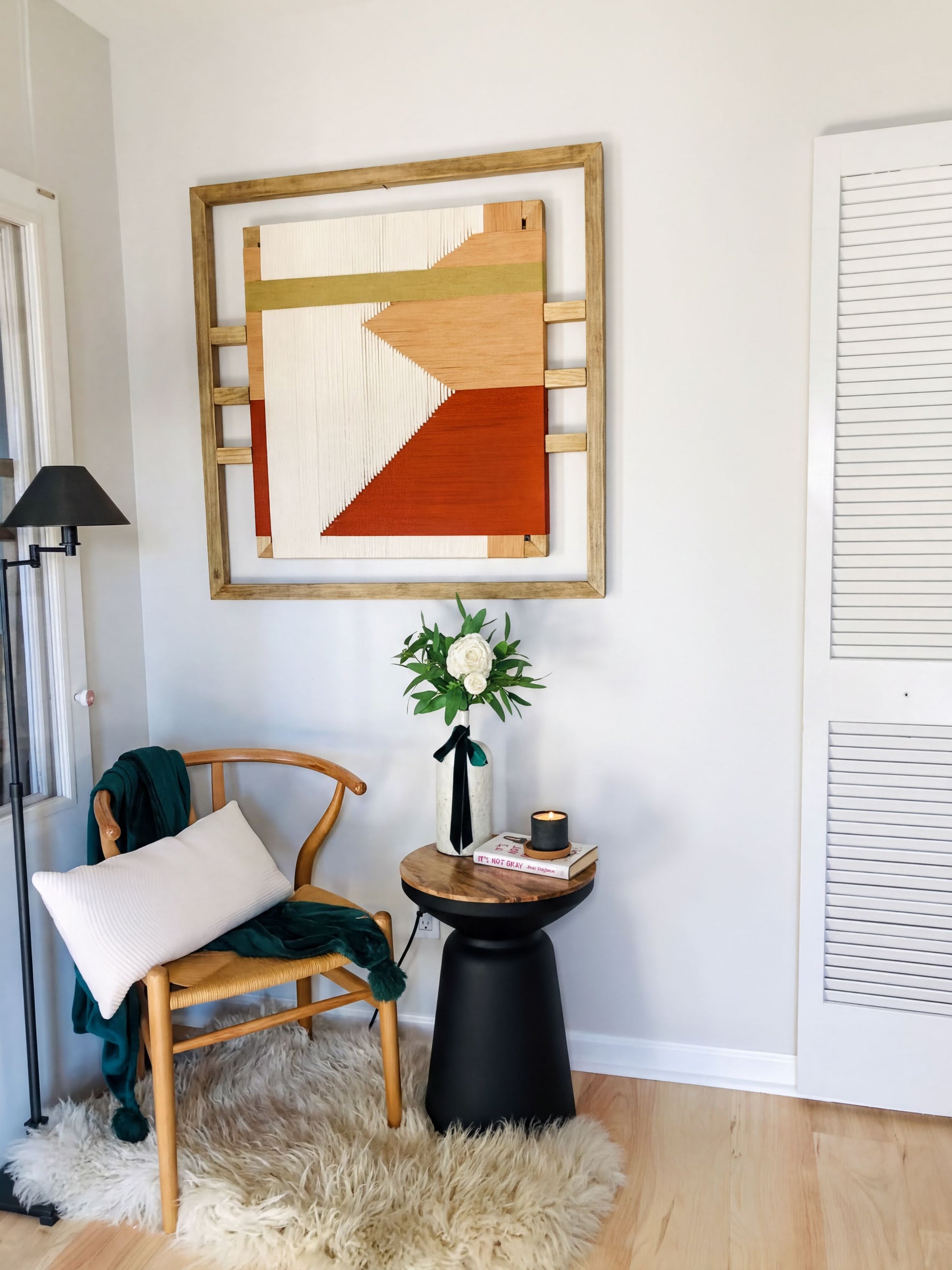 a cozy corner with a wooden chair, a small table with a vase of flowers, and a framed abstract artwork on the wall.