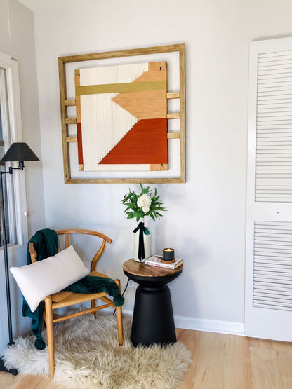 a cozy corner with a wooden chair, a small table with a vase of flowers, and a framed abstract artwork on the wall.