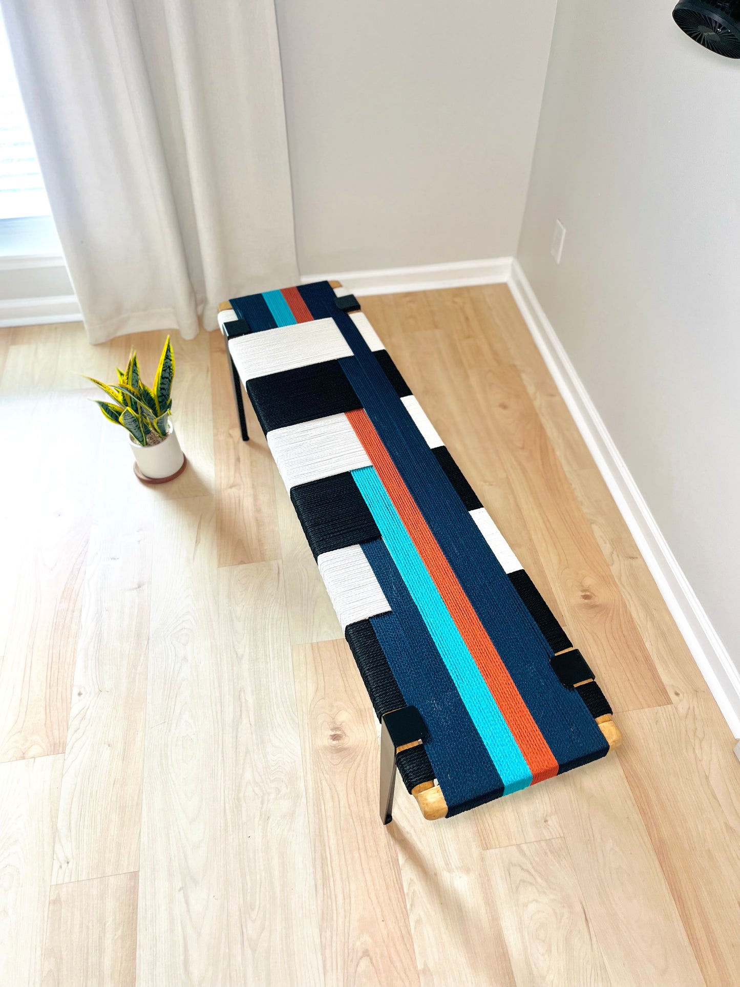 a colorful bench with a geometric pattern of blue, white, and orange stripes, placed on a wooden floor next to a window.