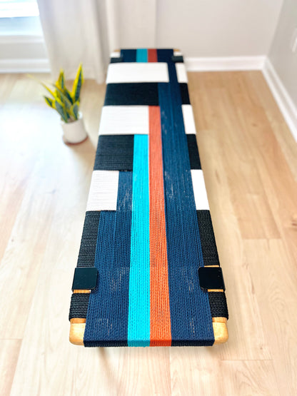 a colorful bench with a black and white striped design, placed on a wooden floor. A potted plant is visible in the background, adding a touch of greenery to the scene.