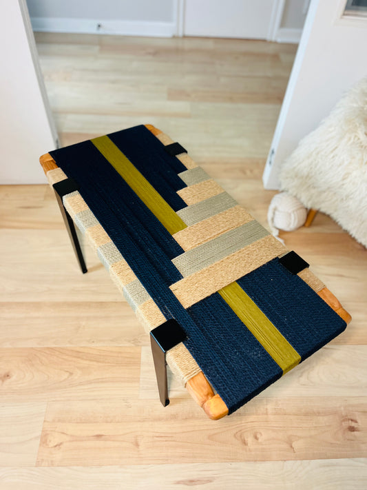a wooden bench with a colorful woven seat, placed on a wooden floor.