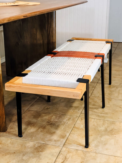 a wooden bench with a woven seat and black metal legs, placed on a tiled floor.